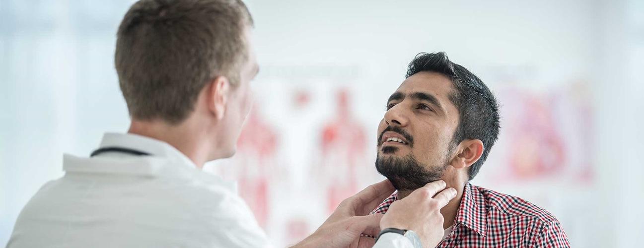 a doctor feels the neck area of male patient to check thyroid