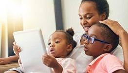 Boy wearing glasses and looking at an iPad with his mother and sister
