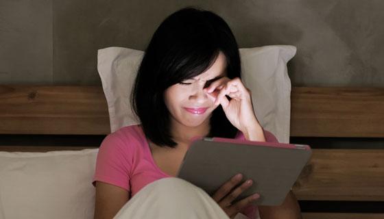 A woman rubs her eye while viewing her mobile tablet device