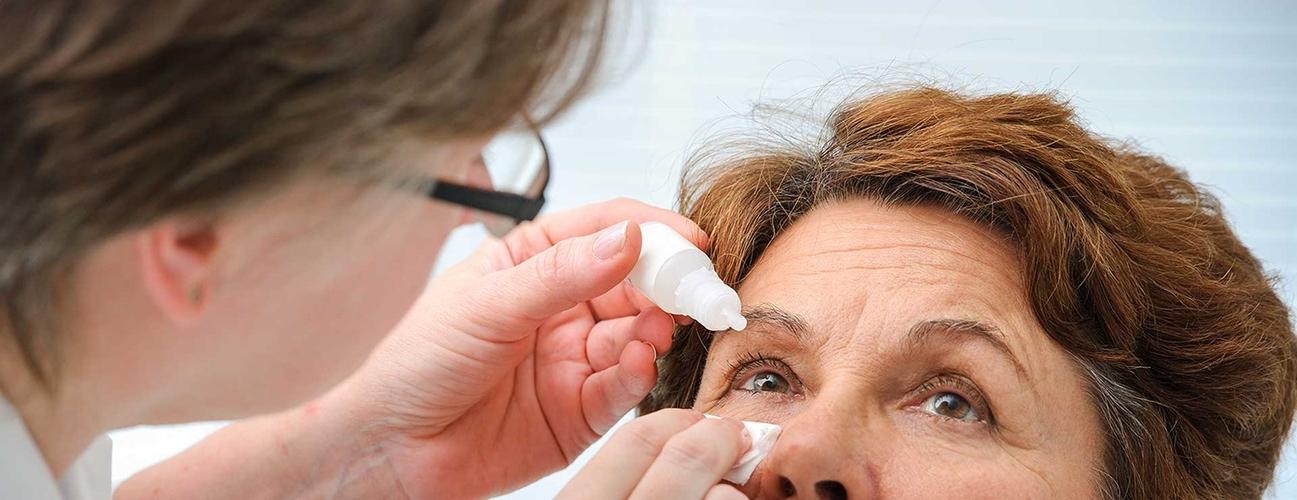 A senior woman receives eye drops from doctor