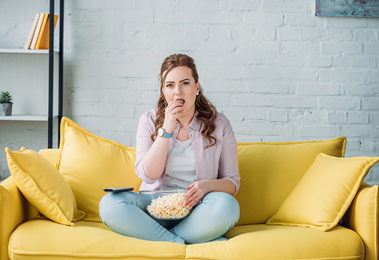 一个女人坐在沙发上，吃着爆米花.